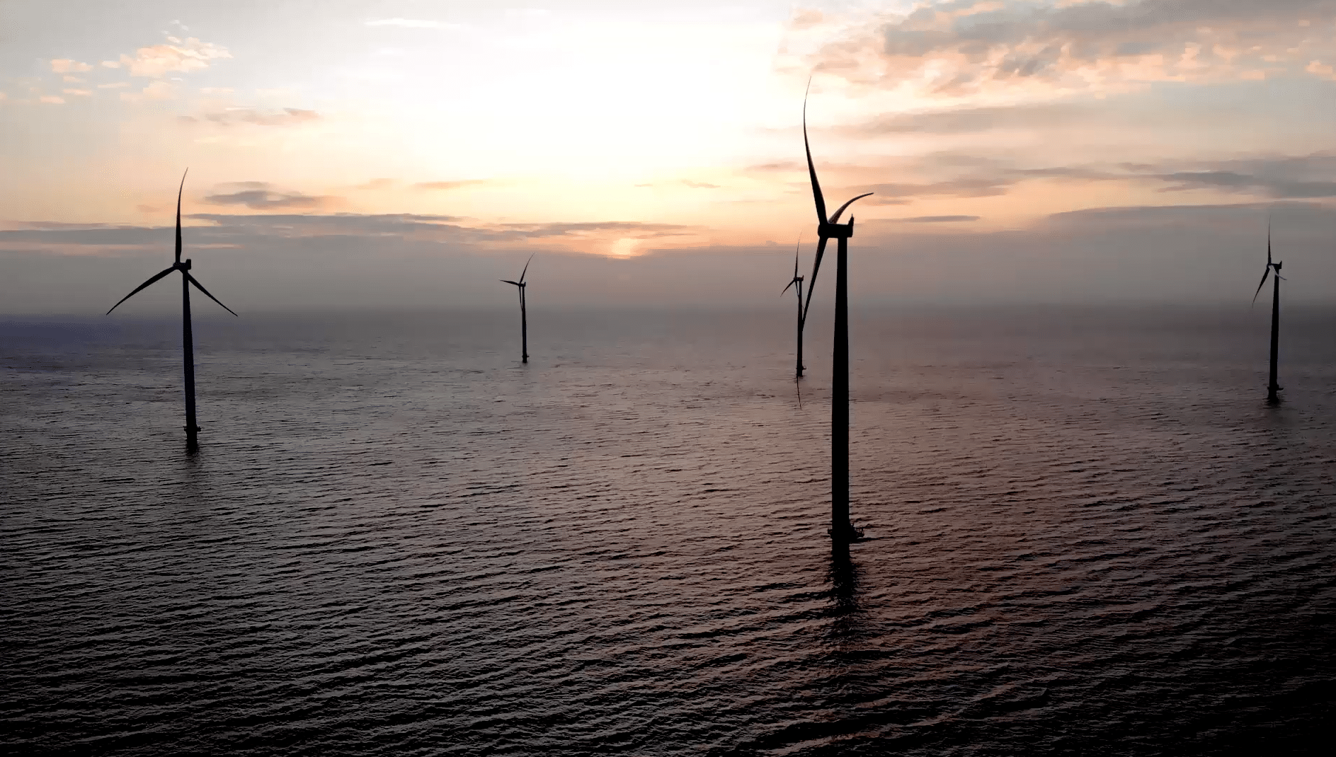 Windmills in the ocean at sunset.